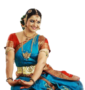 A smiling woman in traditional Indian dance attire, seated.